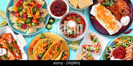 Mexikanische Tischszene. Oben auf einem blauen Holzbanner Hintergrund. Tacos, Burrito-Teller, Nachos, Enchiladas, Tortilla-Suppe und Salat. Kopierbereich. Stockfoto