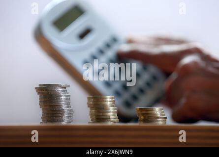 Kaufbeuren, Deutschland. Mai 2024. ABBILDUNG Eine Hand hält einen Taschenrechner hinter drei Stapel Euro-Münzen. Quelle: Karl-Josef Hildenbrand/dpa/Alamy Live News Stockfoto