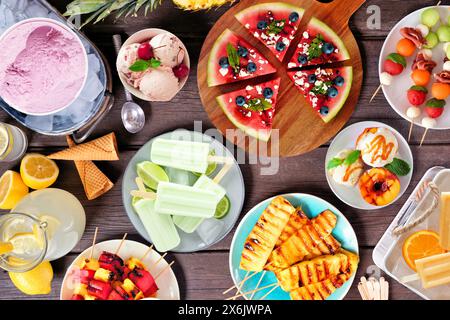 Erfrischende Sommer-Essensszene. Verschiedene gegrillte Früchte, Eis und Eis-Pops. Blick über dem Hintergrund aus dunklem Holz. Stockfoto