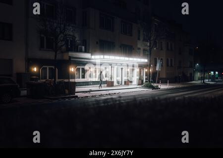 Ein einsamer Mann geht in die Dunkelheit. Beleuchtet durch das Licht des Hotels. Aufgenommen in der Nacht in Koblenz, Deutschland Stockfoto