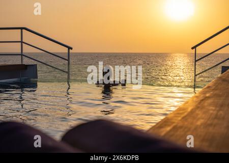 Frau, die sich im Swimmingpool auf dem Achterdeck des Expeditionskreuzfahrtschiffs SH Diana (Swan Hellenic) bei Sonnenuntergang, auf dem Meer, in der Nähe des Jemen, Naher Osten, entspannt Stockfoto