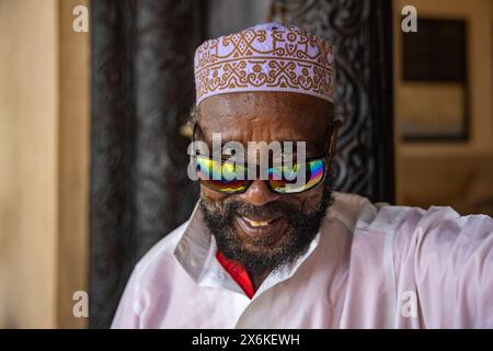 Lächelnder Mann mit muslimischem Taqiyah-Hut und farbenfroher reflektierender Sonnenbrille, Lamu Island, Kenia, Afrika Stockfoto