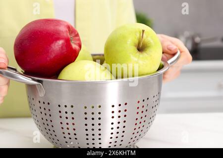 Frau, die Sieb mit frischen Äpfeln am Tisch drinnen hält, Nahaufnahme Stockfoto