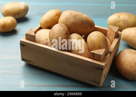 Rohe frische Kartoffeln in Kiste auf hellblauem Holztisch Stockfoto