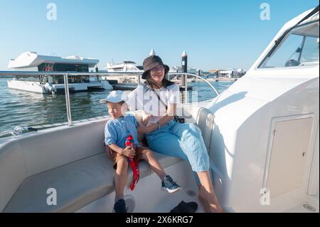 Ein kleiner Junge macht eine Bootsfahrt mit seiner Mutter am Al Bandar Marina in der Nähe von Yas Island, mit der Skyline von Abu Dhabi im Hintergrund könnte es sich um ein Asien handeln Stockfoto