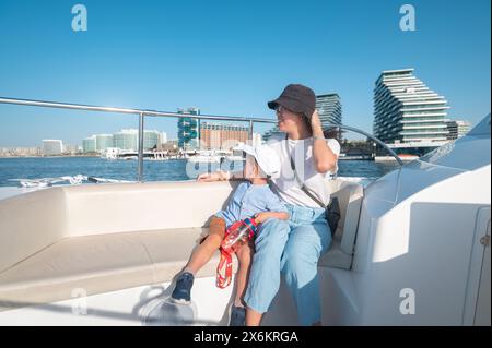 Ein kleiner Junge macht eine Bootsfahrt mit seiner Mutter am Al Bandar Marina in der Nähe von Yas Island, mit der Skyline von Abu Dhabi im Hintergrund könnte es sich um ein Asien handeln Stockfoto