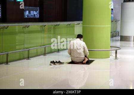 Muslimischer Mann zog seine Schuhe aus und kniete auf einem Gebetsteppich, betend im Maskat International Airport Oman Stockfoto