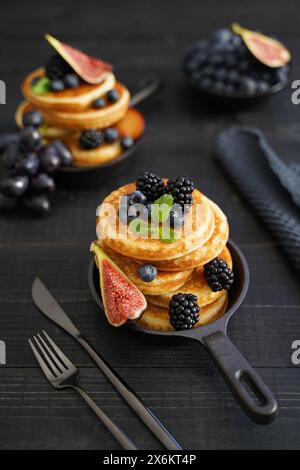 Goldbraune Pfannkuchen vor einem eleganten schwarzen Holzhintergrund mit saftigen Beeren, die Wärme und Genuss ausstrahlen Stockfoto