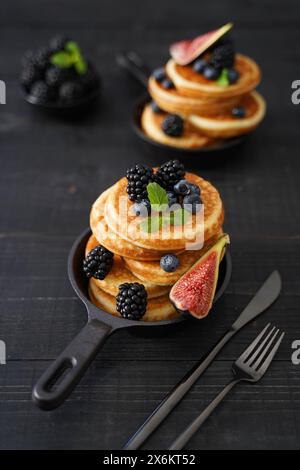 Goldbraune Pfannkuchen vor einem eleganten schwarzen Holzhintergrund mit saftigen Beeren, die Wärme und Genuss ausstrahlen Stockfoto