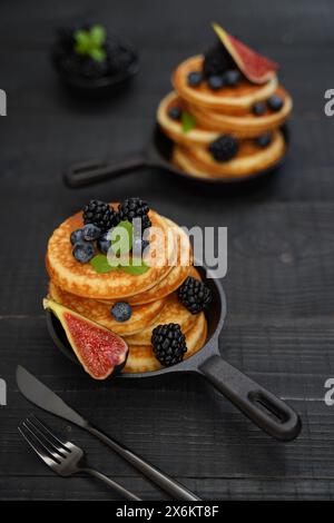 Goldbraune Pfannkuchen vor einem eleganten schwarzen Holzhintergrund mit saftigen Beeren, die Wärme und Genuss ausstrahlen Stockfoto