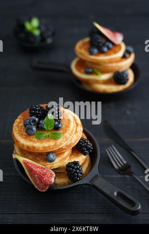 Goldbraune Pfannkuchen vor einem eleganten schwarzen Holzhintergrund mit saftigen Beeren, die Wärme und Genuss ausstrahlen Stockfoto