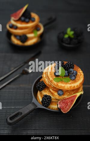 Goldbraune Pfannkuchen vor einem eleganten schwarzen Holzhintergrund mit saftigen Beeren, die Wärme und Genuss ausstrahlen Stockfoto