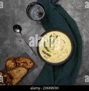 Cremeweiße Spargelsuppe auf dunkelgrauem Steinhintergrund, umgeben von grünem Küchentuch Stockfoto