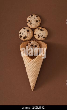 Eisbecher mit Schokoladenkeksen auf braunem Hintergrund. Minimales Konzept für süße Speisen. Kreative Idee für den Sommer. Leckere Schokoladen-Kekse-Chips. Stockfoto