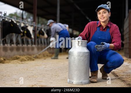 Junglandwirte mit positivem Befund, die während der Arbeit im Milchbetrieb in der Nähe des Stalls mit Kühen Milchkräuter befördert Stockfoto