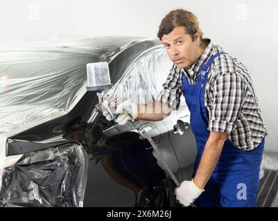 Mann mittleren Alters mit Spritzpistole, um Auto in der Werkstatt zu lackieren Stockfoto