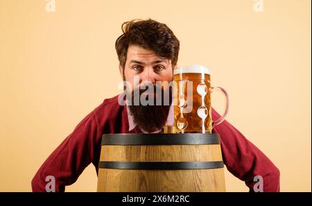 Bierzeit. Ernsthafter bärtiger Mann mit Bier vom Fass auf Holzfässern. Urlaub, Alkohol, Getränke, Freizeit und Menschen Konzept. Oktoberfest. Stilvoll und attraktiv Stockfoto