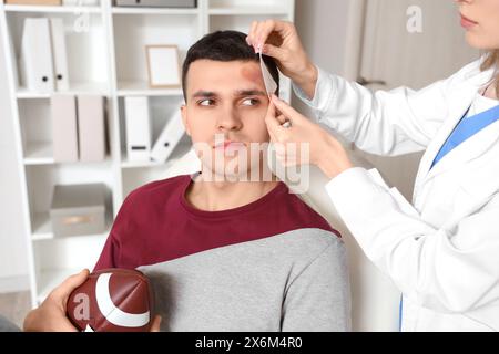 Ärztin, die ein medizinisches Pflaster auf den Kopf eines Rugbyspielers mit Gehirnerschütterung in der Klinik aufbringt Stockfoto