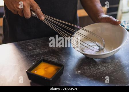 Bakers Hände schlagen Eier mit einem Handrührgerät auf einer weißen Platte, wobei Eigelb von Weißen getrennt wird. Kochen auf traditionelle Weise Stockfoto