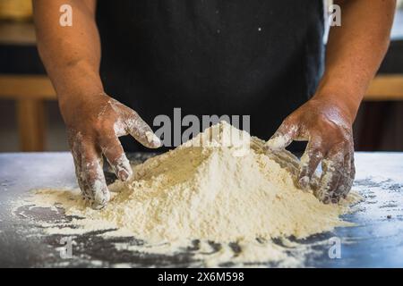 Bakers Hände sind bereit, einen Hügel Mehl zu kneten, isoliert auf schwarzem Hintergrund. Bereitet Brot auf traditionelle Weise zu Stockfoto