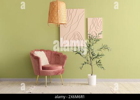 Pinkfarbener Sessel und Olivenbaum in der Nähe der grünen Wand Stockfoto
