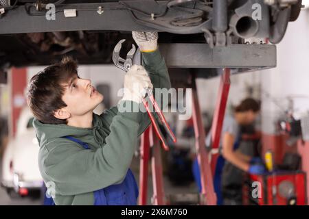 Junger Automechaniker, der in der Werkstatt das Fahrwerk repariert Stockfoto