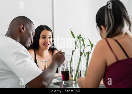 latina, die glücklich lächelt, während sie mit ihren Freunden isst, redet und abhängt, interrassisches Paar Stockfoto