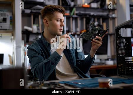 Ein selbstbewusster kaukasischer Techniker oder Techniker stellt den Laptop wieder her und untersucht die Details der Teile des demontierten Laptops. Elektronische Reparaturwerkstatt, Technologiesanierung, Geschäft, Konzeptreparaturen. Stockfoto