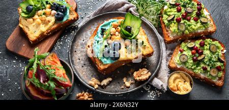 Vegetarische Toasts mit Hummus, Heidelbeere, Avocado, Tomate. Köstliches veganes Frühstück auf dunklem Hintergrund. Banner Stockfoto