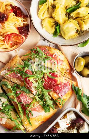 Vollständiger Tisch mit italienischen Gerichten auf Tellern Pizza, Pasta, Ravioli, Salat und Focaccia auf weißem Hintergrund. Draufsicht Stockfoto
