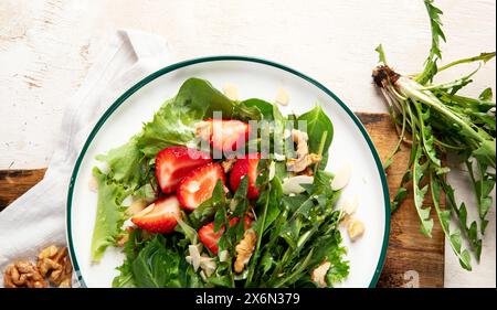 Löwenzahn-Salat mit Erdbeere und Wallnüssen in Teller auf weißem Hintergrund, Blick von oben. Panorama mit Kopierbereich. Stockfoto