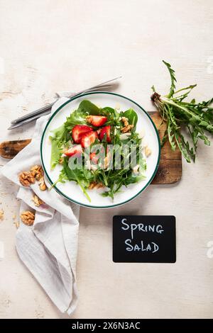 Löwenzahn-Salat mit Erdbeere und Wallnüssen in Teller auf weißem Hintergrund, Blick von oben. Stockfoto