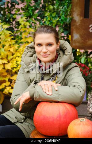 Schöne Frau, die auf einem Herbstmarkt sitzt, mit der Hand auf einem Kürbis auf dem Tisch Stockfoto