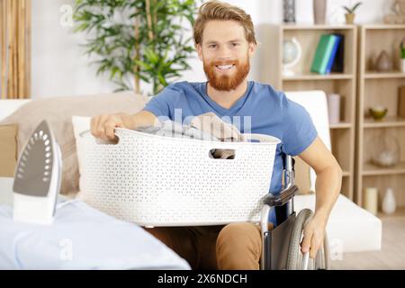 Mann im Rollstuhl, der die Wäsche aus der Waschmaschine holt Stockfoto