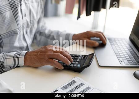 Glücklicher erfolgreicher Geschäftsmann, der am Arbeitsplatz Gewinne zählt. Mit Laptop, Rechner, Scheck, Rechnung, Rechnung, Einkünfte zählen, finanzielle Genüsse genießen Stockfoto