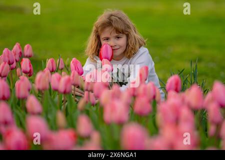 Junge im FrühlingsTulpenblütenpark. Glückliche Kindheit. Frühlingsferien. Entzückendes Kind, das Tulpen im Frühlingsgarten riecht. Süßer kleiner Junge in einer Blüte Stockfoto