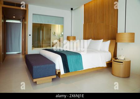 Ein luxuriöses, aber minimalistisches Schlafzimmer mit einem komfortablen Bett mit makellos weißer Bettwäsche und einem hölzernen Kopfteil. Stockfoto