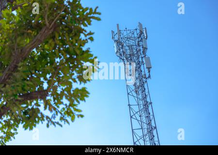 Außenbereich 5g-Kommunikationsturm digitales drahtloses Funksignal Fernübertragungszelle am blauen Himmel mit grünem Baum Stockfoto