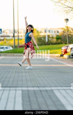 Eine lebendige junge Frau mit lockigen Haaren tanzt fröhlich auf einem Stadtrand und hebt ihre Hand in die Luft. Stockfoto