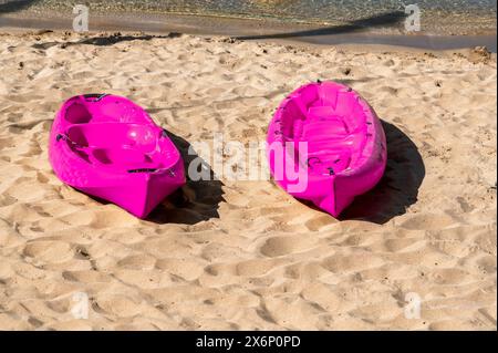 Pinkfarbene Plastikkanus, die am sonnigen Tag am Sandstrand liegen Stockfoto