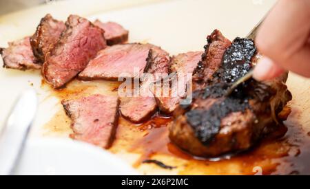 Eine Person schneidet sorgfältig ein wunderschön gekochtes Steak, das seine zarte, rosa Mitte enthüllt. Der Schwerpunkt liegt auf der Textur und Sukkulenz des Fleisches Stockfoto