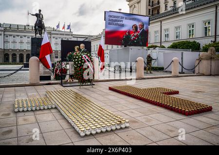 Warschau, Mazovia, Polen. April 2024. Vor dem Präsidentenpalast werden Kerzen angezündet und Blumenkränze stehen vor einem Banner des verstorbenen Präsidenten und seiner Frau. Polen erinnert an den 14. Jahrestag der Flugunglücke in Smole?SK, bei der der polnische Präsident Lech Kaczy?Ski, seine Frau Maria und 94 weitere Würdenträger und Crew ums Leben kamen. Angesichts der Gegenpathie zwischen der Partei Recht und Gerechtigkeit unter der Führung von Kaczy?Skis Zwillingsbruder Jaros?aw und der Bürgerkoalition unter der Leitung des aktuellen polnischen Ministerpräsidenten Donald Tusk, wird der Jahrestag nun öffentlich begangen Stockfoto