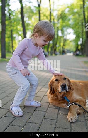 Kind mit Hund. Kinderschläge Labrador Retriever Hund auf Kopf im Park. Tierpflege. Stockfoto