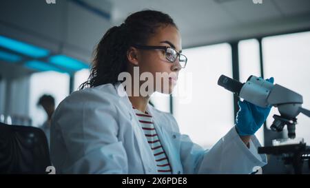 Medizinisches Wissenschaftslabor: Schöner schwarzer Wissenschaftler verwendet Mikroskop und macht Analyse der Testprobe. Vielfältiges Team von jungen Spezialisten, die fortschrittliche Technologie verwenden. Stockfoto