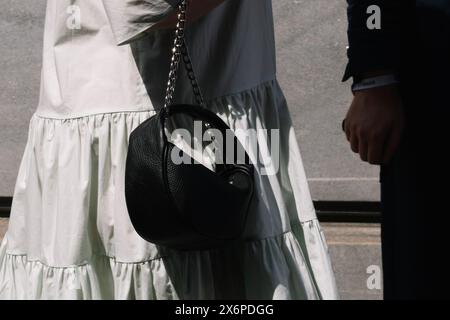 Mailand, Italien - 20. Juni 2022: Schwarze Ledertasche mit silberner Kette im Kontrast zu einem leichten, fließenden Kleid in sonnendurchflutetem urbanem Ambiente Stockfoto