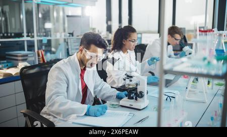 Medical Science Laboratory: Reihe von verschiedenen Team von Multi-ethnischen jungen Wissenschaftlern, die unter Mikroskop suchen, Chemikalien analysieren, reden, Probleme lösen. Biotechnologiespezialisten, die im Advanced Lab arbeiten Stockfoto