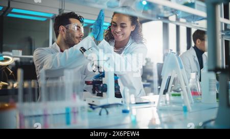 Modernes medizinisches Forschungslabor: Porträt lateinischer, schwarzer junger Wissenschaftler mit Mikroskop und Giving High Five nach erfolgreichem Ergebnis. Ein vielseitiges Team von Spezialisten arbeitet im Advanced Lab Stockfoto