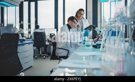 Modernes medizinisches Forschungslabor: Aufnahme von zwei jungen Wissenschaftlern mit Pipette, Digital Tablet, Probenanalyse, Sprechen. Ein vielseitiges Team von Spezialisten arbeitet im Advanced Bio Technology Lab Stockfoto