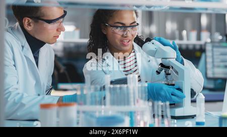 Modernes medizinisches Forschungslabor: Porträt von schwarzen und kaukasischen jungen Wissenschaftlern mit Mikroskop, Digital Tablet, Sample Analysis, Talking. Ein vielseitiges Team von Spezialisten arbeitet im Advanced Lab Stockfoto
