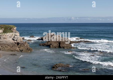 Eine malerische Küste mit felsigen Formationen, klarem blauem Wasser, rauschenden Wellen und einer Klippe mit Grün unter klarem Himmel Stockfoto